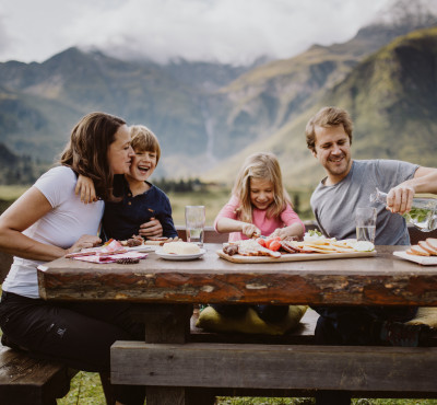 Eine glückliche Familie mit einer tollen Jausen beim Wandern. So kann ein Familienurlaub im Hotel Palace aussehen